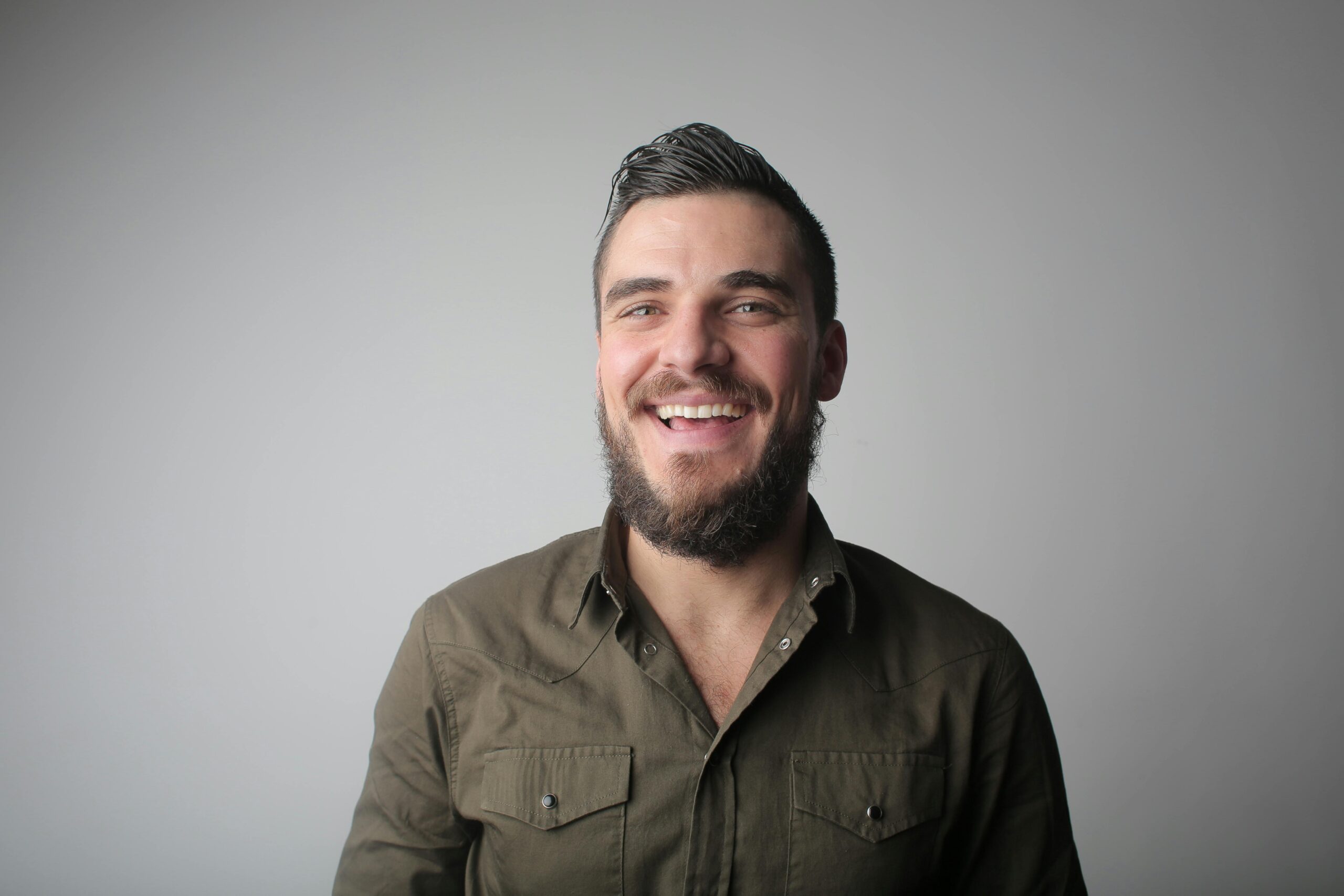 Portrait of a bearded man smiling joyfully in a casual studio setting.